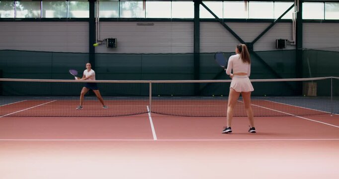 Two girls hitting the ball with their rackets on a tennis court. Two female tennis players play a training match on the court.