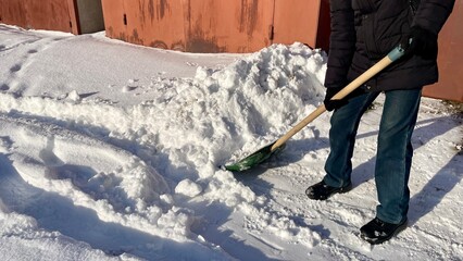 Naklejka premium Man clearing fresh white snow with a green shovel in winter courtyard, close up of snow removal process