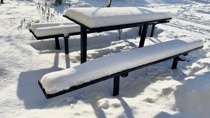 Wooden picnic table and benches covered with deep fresh snow in a sunny winter park