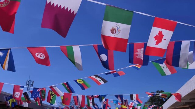 Various national flags of the world hang on strings, fluttering in the breeze against a clear blue sky. A vibrant display of global unity and international diversity at an outdoor event