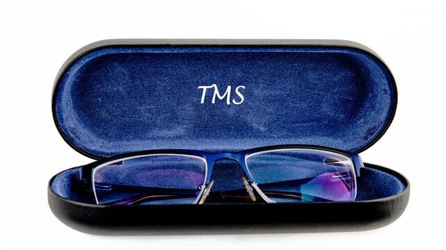 A pair of sophisticated blue eyeglasses rest delicately inside a plush, dark blue protective case. The initials TMS are emblazoned on the interior of the case