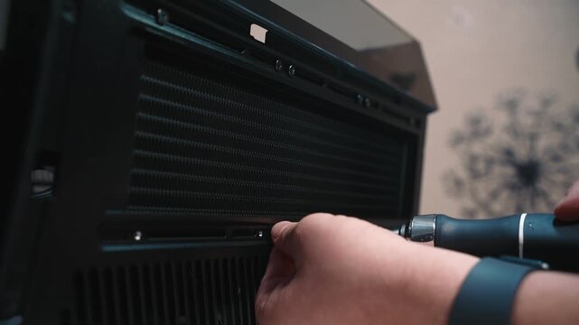 Tightening screw while installing cooling radiator into case, detailed close-up of hand with screwdriver securing component inside black computer chassis
