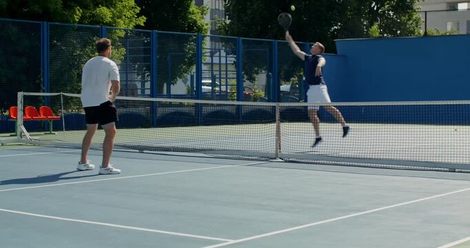 Two tennis players practice hitting the ball with rackets in a sparring match.. Two male tennis players train on the court with rackets in hand.