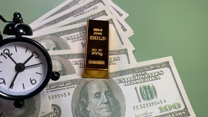 Alarm clock beside a gold bar and U.S. hundred-dollar bills, highlighting time’s role in financial growth © MR HEPPY
