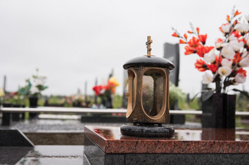 Lantern on tombstone with colorful flowers in rainy cemetery scene
