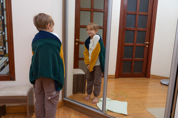 Young boy looking at reflection in mirror trying on jacket. Child getting dressed at home © Victor zastol'skiy