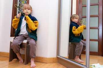 Little boy playing with a green hanger near a mirror. Child sitting on a stool indoors © Victor zastol'skiy