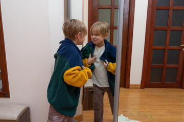 Funny young boy making a grimace in the mirror. Child trying on a colorful fleece jacket © Victor zastol'skiy