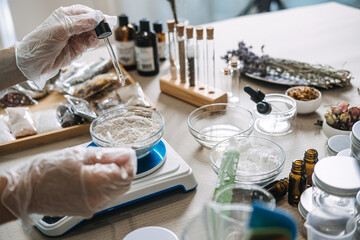 Hands in gloves use glass dropper to add liquid to bowl of powder on digital scale. Phytochemistry,...