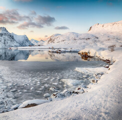 Flakstadpollen and Boosen fjords with cracks on ice during sunrise with Hustinden mountain on background.