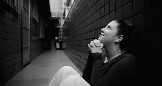 Woman sitting on floor in narrow corridor praying for help during difficult times, hope amid struggle, faith, surrender, emotional vulnerability, spiritual resilience, black and white
