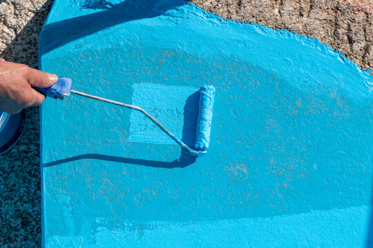 Pintor aplicando revestimento de resina azul numa superf&iacute;cie de piscina com um rolo de l&atilde; durante o processo de renova&ccedil;&atilde;o e manuten&ccedil;&atilde;o