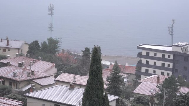 Static shot of snow covered rooftops and trees overlooking the Adriatic Sea during active snowfall in Rijeka