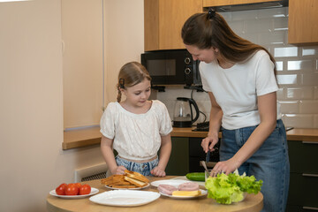 Mother and daughter bonding in a modern kitchen, learning to prepare healthy sandwiches together...