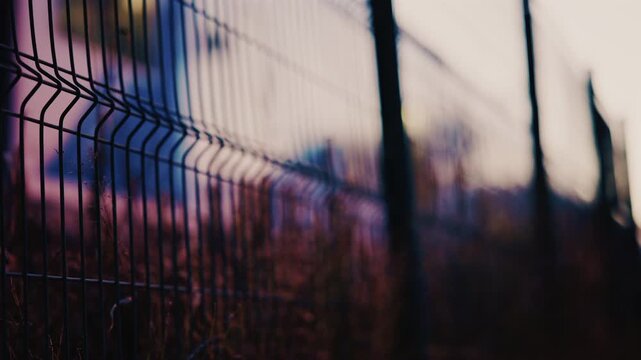 Close up of a metal fence with softly blurred lights of a train passing in the background at dusk