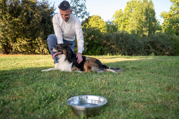 Man petting border collie in park with water bowl