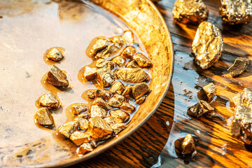 Gold nuggets on a brass plate on a wooden tabletop. Imitation gold nuggets.