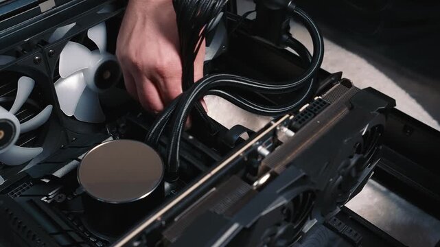 Connecting power cables to motherboard during PC build, close-up of male hand routing braided wires to connectors near the cooling system and graphics card
