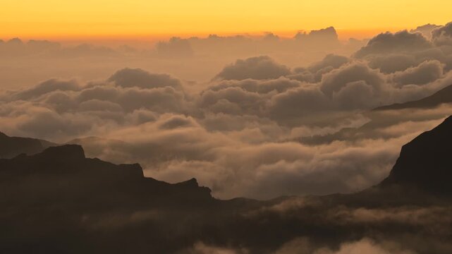 Timelapse dramatic clouds glowing with warm sunset colors after the sun has set, filmed from Pico do Arieiro in mountains Madeira Island, Portugal. Clouds below peaks move rapidly and change shape