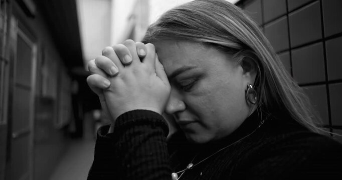 Middle aged woman praying in narrow urban passage seeking divine help faith and spiritual strength during personal crisis expressing hope surrender and inner struggle