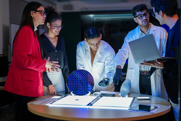 Specialist team of engineers and executives inspecting a large silicon wafer in a high-tech semiconductor laboratory. Discussion on microchip and RAM memory manufacturing process and quality control.