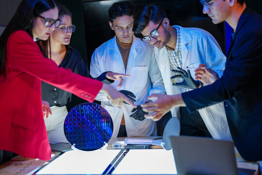 engineering research group analyzing a silicon wafer prototype. Professors and students collaborating on a microchip physics experiment in laboratory to develop future electronic technology.