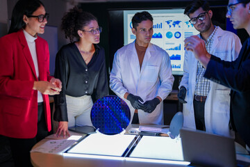 Specialist team of engineers and executives inspecting a large silicon wafer in a high-tech semiconductor laboratory. Discussion on microchip and RAM memory manufacturing process and quality control.