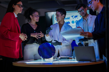 Specialist team of engineers and executives inspecting a large silicon wafer in a high-tech semiconductor laboratory. Discussion on microchip and RAM memory manufacturing process and quality control.