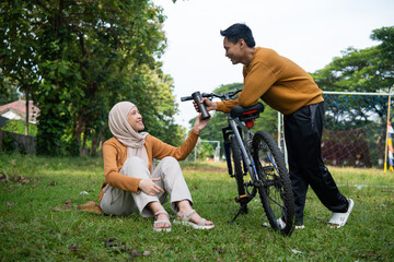 Fototapeta premium Asian couple sharing moment together at the park after cycling and the man handing her a bottle of water.