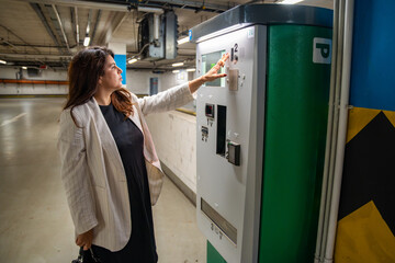 Woman paying for parking at automated payment machine in public parking garage. Everyday urban...