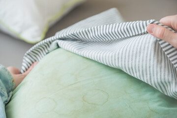 Female hands removing pillowcase from pillow in a living room. Dirty stains sweat or saliva on a green pillow. Conscious home care and sustainable living concept. top view