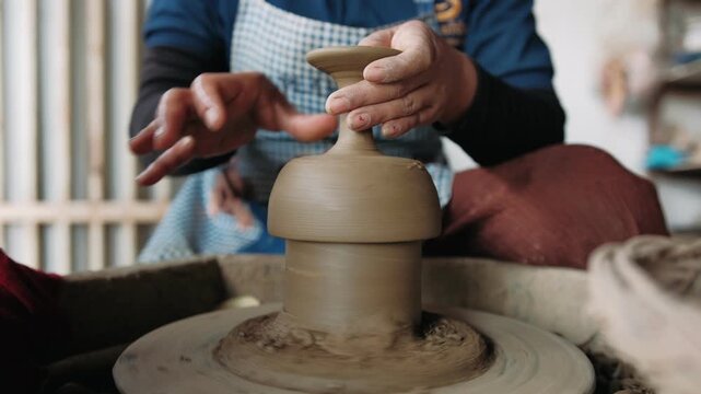 Close up of a potter hands shaping a piece of wet clay spinning on a pottery wheel, creating a ceramic vase in a workshop. Working process in ceramic workshop. Handmade concept. Siem Reap, Cambodia.