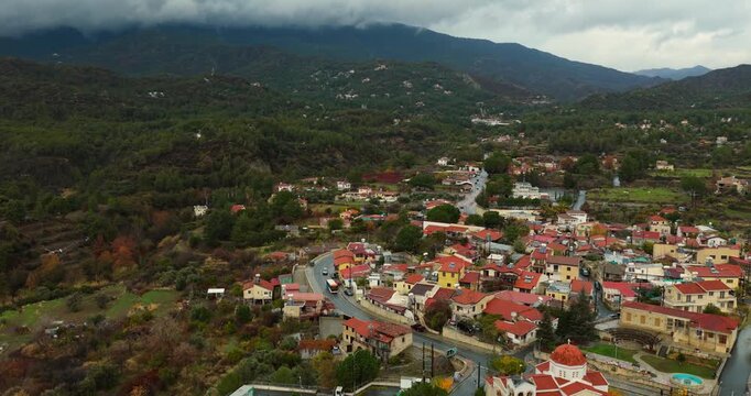 Drone backward flyover above Trimiklini village with road traffic and Troodos Mountains