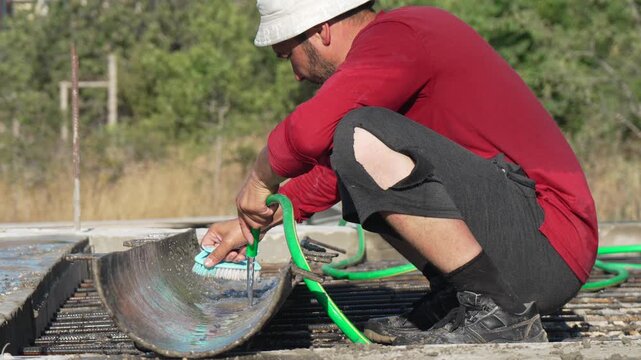 Construction worker cleaning half-pipe formwork preparing concrete pour