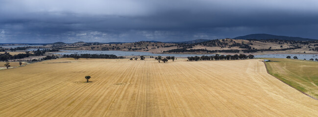 Aerial panorama view of heavy rain falling from dark clouds over a rural lake behind dry farmland
