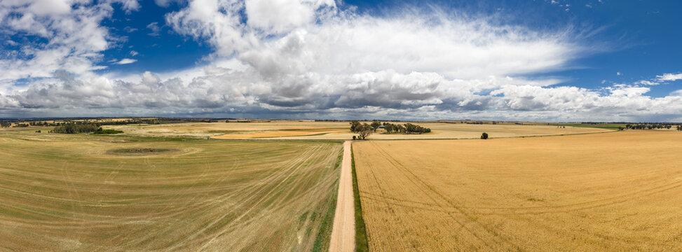 Aerial panorama view of a narrow gravel road on farmland heading towards stormclouds in the distance