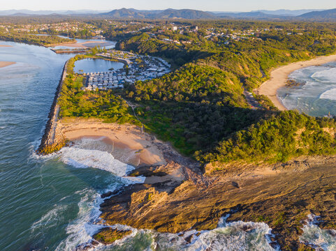 Aerial view of waves crashing on large rocky outcrop in golden morning light
