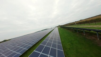 Aerial FPV drone shot skimming above solar power panel arrays in farmland showcasing renewable electricity infrastructure in rural UK