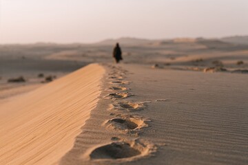 Footprints in sand dunes with lone figure in desert landscape