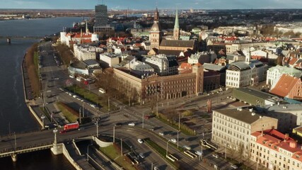 Riga city center traffic at Stone Bridge and 11th November Embankment intersection. Old Town skyline with Dome Cathedral and Saint Peter church spires. Latvia capital Daugava river sunset.