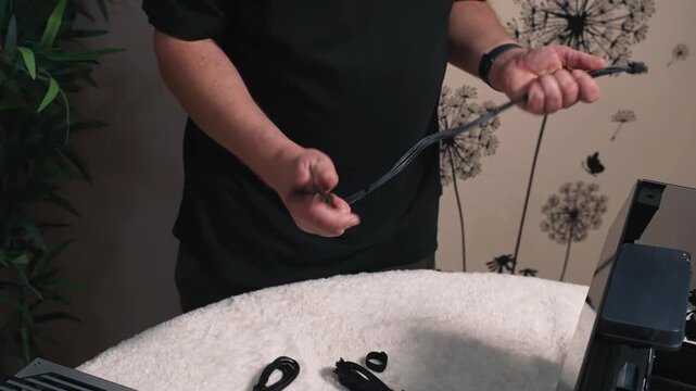 Selecting appropriate power cable for connecting the motherboard, man holds a 24-pin power cable in hands, with part of the PC case 
