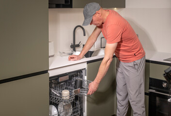 Man doing household chores in a modern kitchen, loading or unloading a dishwasher. Person using the