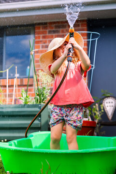 Little girl playing outdoors with hose in backyard wearing big floppy sun hat - water play