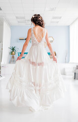 Naklejka premium Elegant woman in a flowing white dress with intricate lace details stands gracefully in a bright, modern interior, showcasing beauty and style in a serene atmosphere
