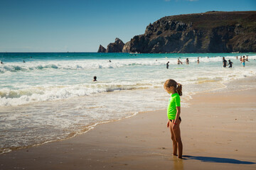 Child girl with green t-shirt standing in Pen Hat beach on the atlantic coast in Camaret-sur-Mer. Finistere, Brittany, France. Profile portrait.
