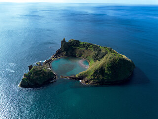 Aerial view of a spectacular volcanic island crater surrounded by the blue ocean. © Iván López
