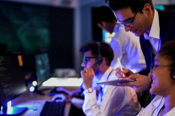 Professional financial trading team analyzing stock market trends in a modern office. Brokers with headsets discuss global investment strategies on a digital tablet at night.