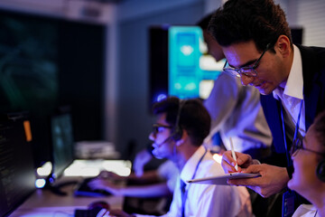 Professional financial trading team analyzing stock market trends in a modern office. Brokers with headsets discuss global investment strategies on a digital tablet at night.