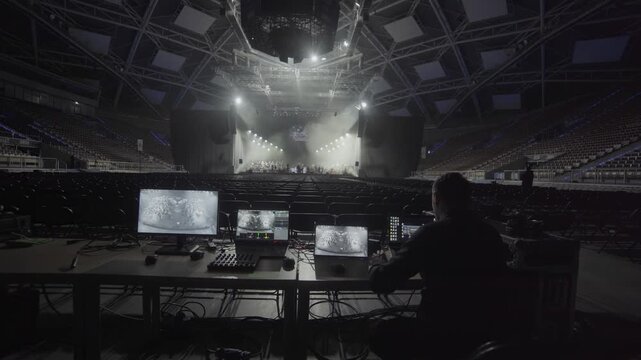 Light engineer monitors live feed from multiple screens in dark control zone. Glowing monitors guide technical adjustments during test phase