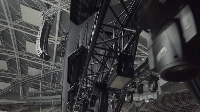 Lighting equipment hangs from overhead truss structure. Black fixtures align in row preparing stage illumination for upcoming concert